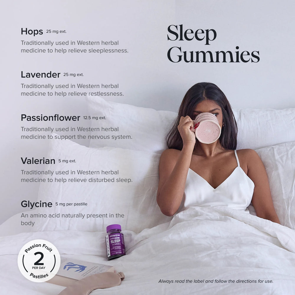 A woman in a white bed wearing a white camisole and drinking from a pink mug, with a purple bottle of novomins sleep gummies beside her. The image includes text listing ingredients (Hops, Lavender, Passionflower, Valerian, Glycine) and the product name 'Sleep Gummies'.